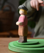 Ostheimer son wooden toy figure placed on a green meadow grass play bases, a child can be seen pointing at it in the background.