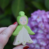 An Ostheimer hand made and hand painted wooden snowdrop Flower Child figure toy held in an adult's hand for scale. These flower child wooden figures are part of a wide range of expertly hand crafted wooden toys here at Babipur. 
