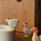 Ostheimer white standing hen placed on the edge of a village well with a hen and rooster standing besides it.