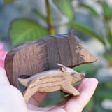 An Ostheimer wild boar sow wooden toy figure shown in an adult's hand for scale, a piglet ca be seen in the foreground. Check out our full range of expertly handcrafted wooden toys here at Babipur.