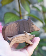 An Ostheimer wild boar sow wooden toy figure shown in an adult's hand for scale, a piglet ca be seen in the foreground. Check out our full range of expertly handcrafted wooden toys here at Babipur.