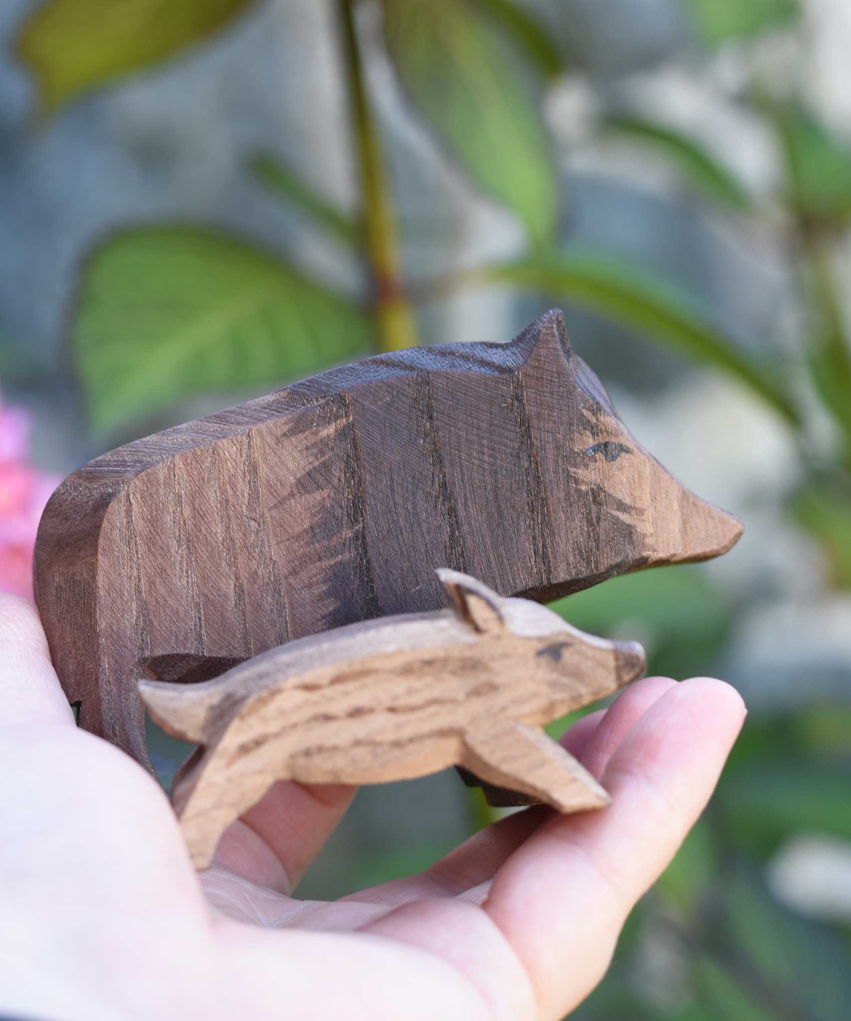 An Ostheimer wild boar sow wooden toy figure shown in an adult's hand for scale, a piglet ca be seen in the foreground. Check out our full range of expertly handcrafted wooden toys here at Babipur.