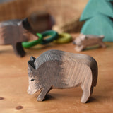 Ostheimer wild boar wooden toy figure placed on a wooden surface with other wild boars and a small spruce tree in the background. 