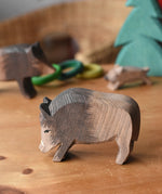 Ostheimer wild boar wooden toy figure placed on a wooden surface with other wild boars and a small spruce tree in the background. 