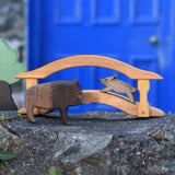 Ostheimer wild boar sow and piglet wooden toy figures placed on a wooden toy bridge in a small world play scene set up on a stone wall outdoors. Ostheimer green grass and an Oak tree can be seen off to the side of the scene.. 