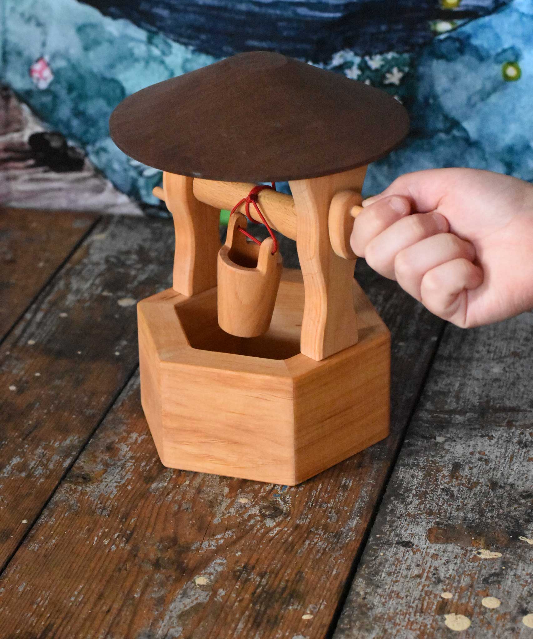 A child's hand winding up the bucket on the Ostheimer wooden wishing well toy. These wooden figures are part of a wide range of expertly hand crafted wooden toys here at Babipur. 