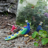 Ostheimer handmade wooden peacock figure with it's feathers closed standing in front of glass. Figure is hand-painted in vibrant blues and greens, made from sustainable wood in Germany and sold at Babipur.