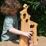 A child playing, standing behind an Ostheimer wooden bell tower. The child is reaching for the princess placed in front of the tower. These wooden figures are part of a large range of expertly hand crafted, Waldorf inspired, wooden toys here at Babipur.