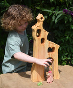 A child playing, standing behind an Ostheimer wooden bell tower. The child is reaching for the princess placed in front of the tower. These wooden figures are part of a large range of expertly hand crafted, Waldorf inspired, wooden toys here at Babipur.