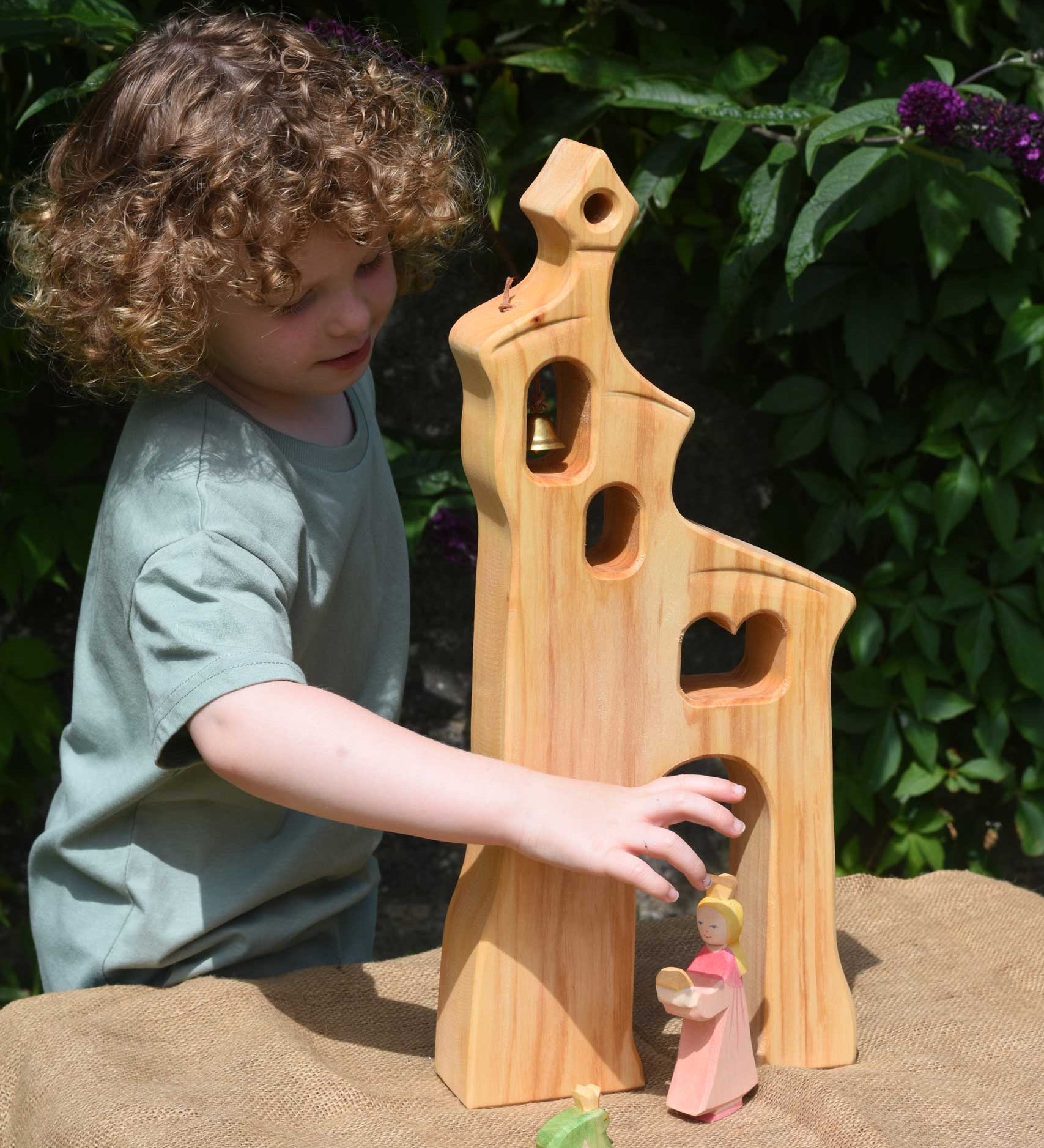 A child playing, standing behind an Ostheimer wooden bell tower. The child is reaching for the princess placed in front of the tower. These wooden figures are part of a large range of expertly hand crafted, Waldorf inspired, wooden toys here at Babipur.