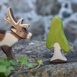 An Ostheimer Wooden Birch Tree Figure placed on a stone wall outdoors.  An Ostheimer wooden reindeer figure can be seen just off to the side.