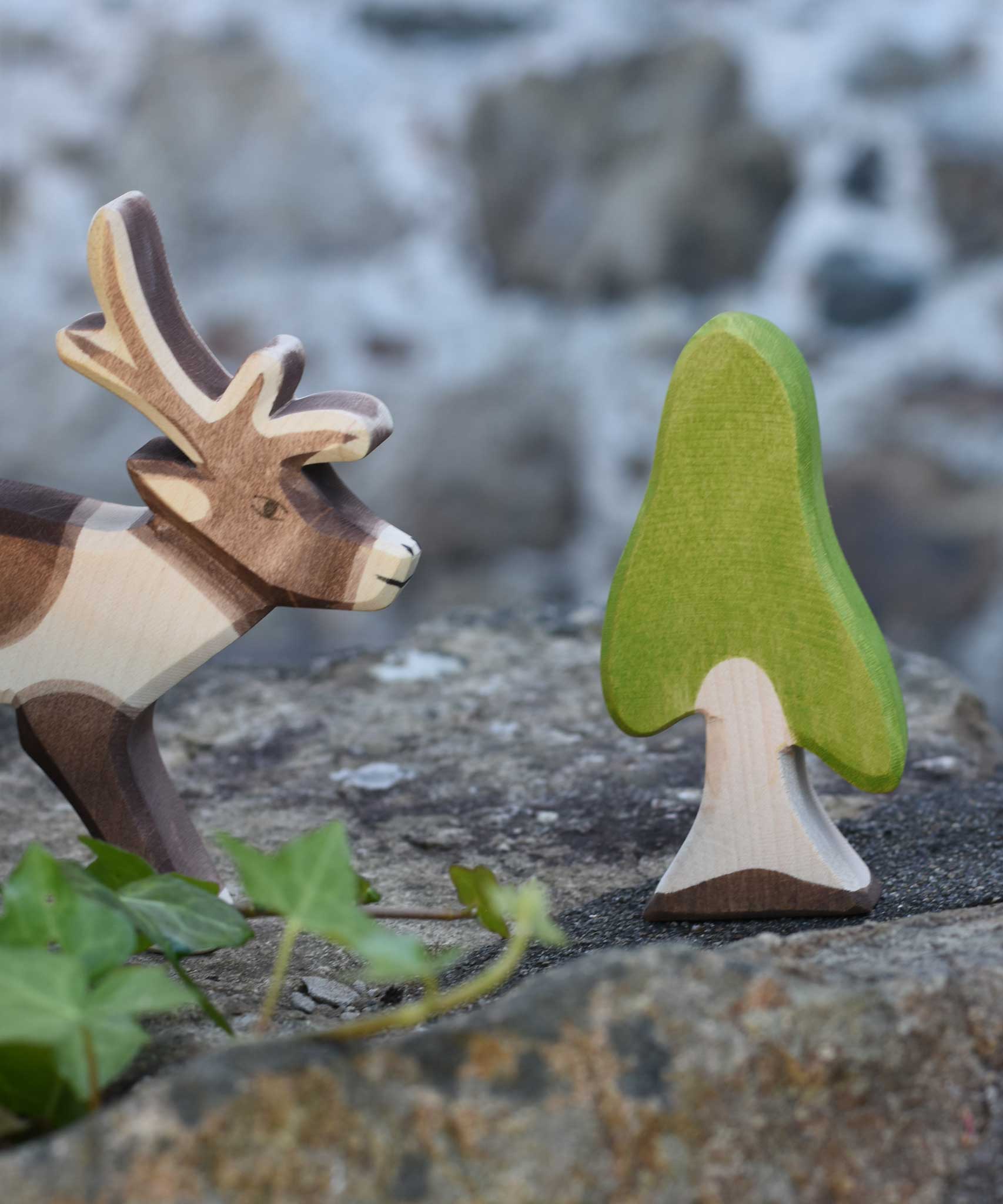 An Ostheimer Wooden Birch Tree Figure placed on a stone wall outdoors.  An Ostheimer wooden reindeer figure can be seen just off to the side.