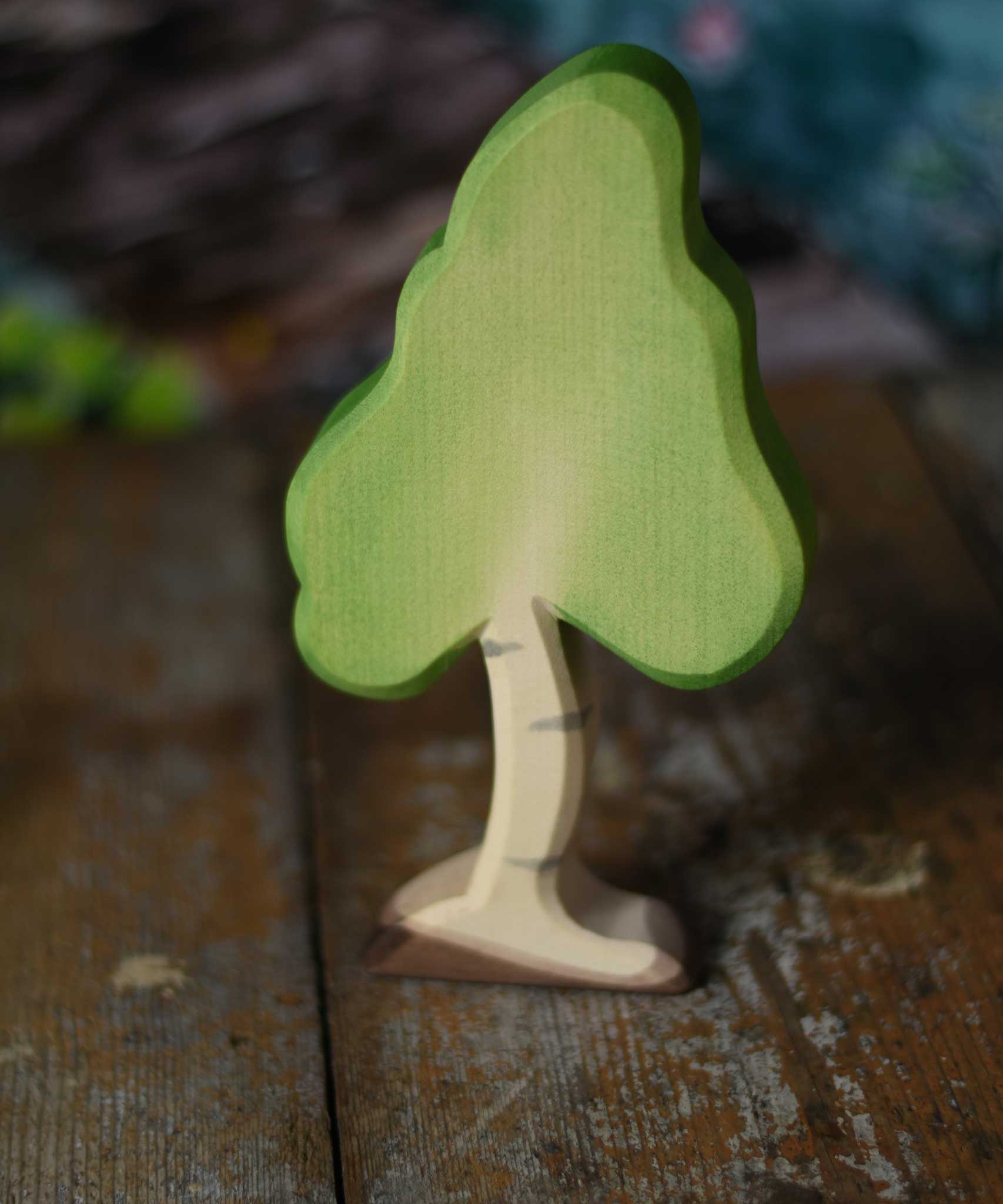 A small Ostheimer birch tree figure placed on a wooden surface. These wooden figures are part of a wide range of expertly hand crafted wooden toys here at Babipur. 