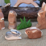Two small Ostheimer rabbit wooden toy figures placed at the front of a small world play scene. One rabbit is  Black and White and the other is brown. Other rabbits from the collection can be seen in the background. Check out our full range of expertly crafted wooden toy figures and scenery here at Babipur.