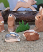 Two small Ostheimer rabbit wooden toy figures placed at the front of a small world play scene. One rabbit is  Black and White and the other is brown. Other rabbits from the collection can be seen in the background. Check out our full range of expertly crafted wooden toy figures and scenery here at Babipur.