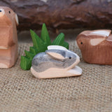 A close up of an Ostheimer Black and White Small Rabbit Wooden Figure placed in a small world play scene. Other Ostheimer rabbits and Ostheimer grass can be seen in the background.  