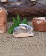 A close up of an Ostheimer Black and White Small Rabbit Wooden Figure placed in a small world play scene. Other Ostheimer rabbits and Ostheimer grass can be seen in the background.  
