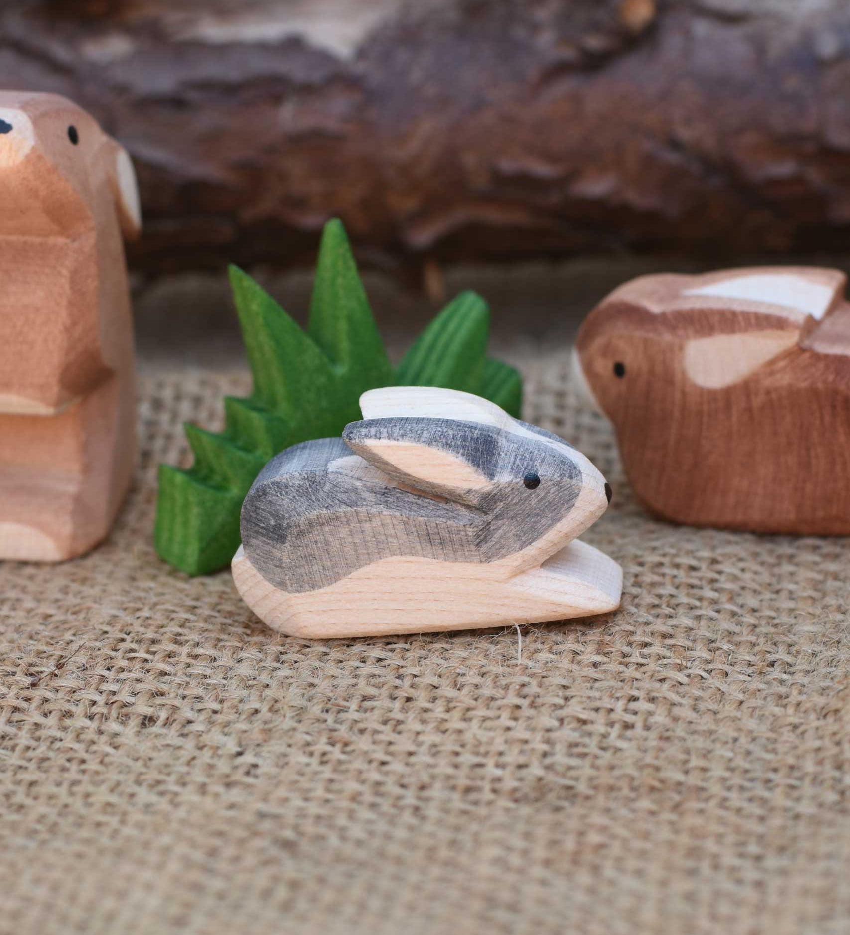 A close up of an Ostheimer Black and White Small Rabbit Wooden Figure placed in a small world play scene. Other Ostheimer rabbits and Ostheimer grass can be seen in the background.  