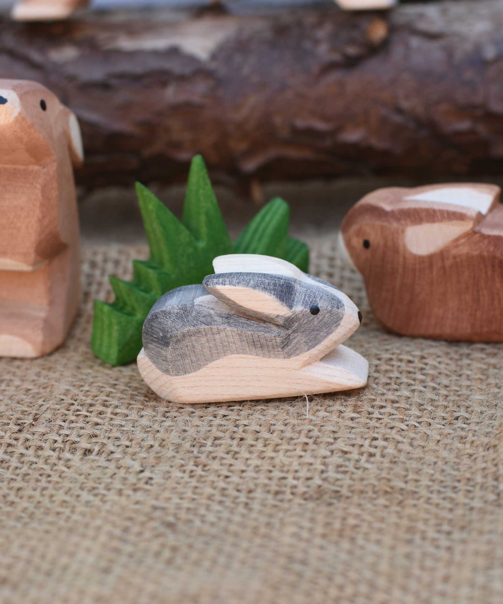 A close up of an Ostheimer Black and White Small Rabbit Wooden Figure placed in a small world play scene. Other Ostheimer rabbits and Ostheimer grass can be seen in the background.  