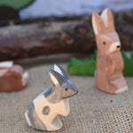 An Ostheimer Black and White Standing Rabbit wooden toy figure placed at the front of a small world play scene. Other Ostheimer rabbits can be seen in the background. Check out our full range of expertly crafted wooden toy figures and scenery here at Babipur. 