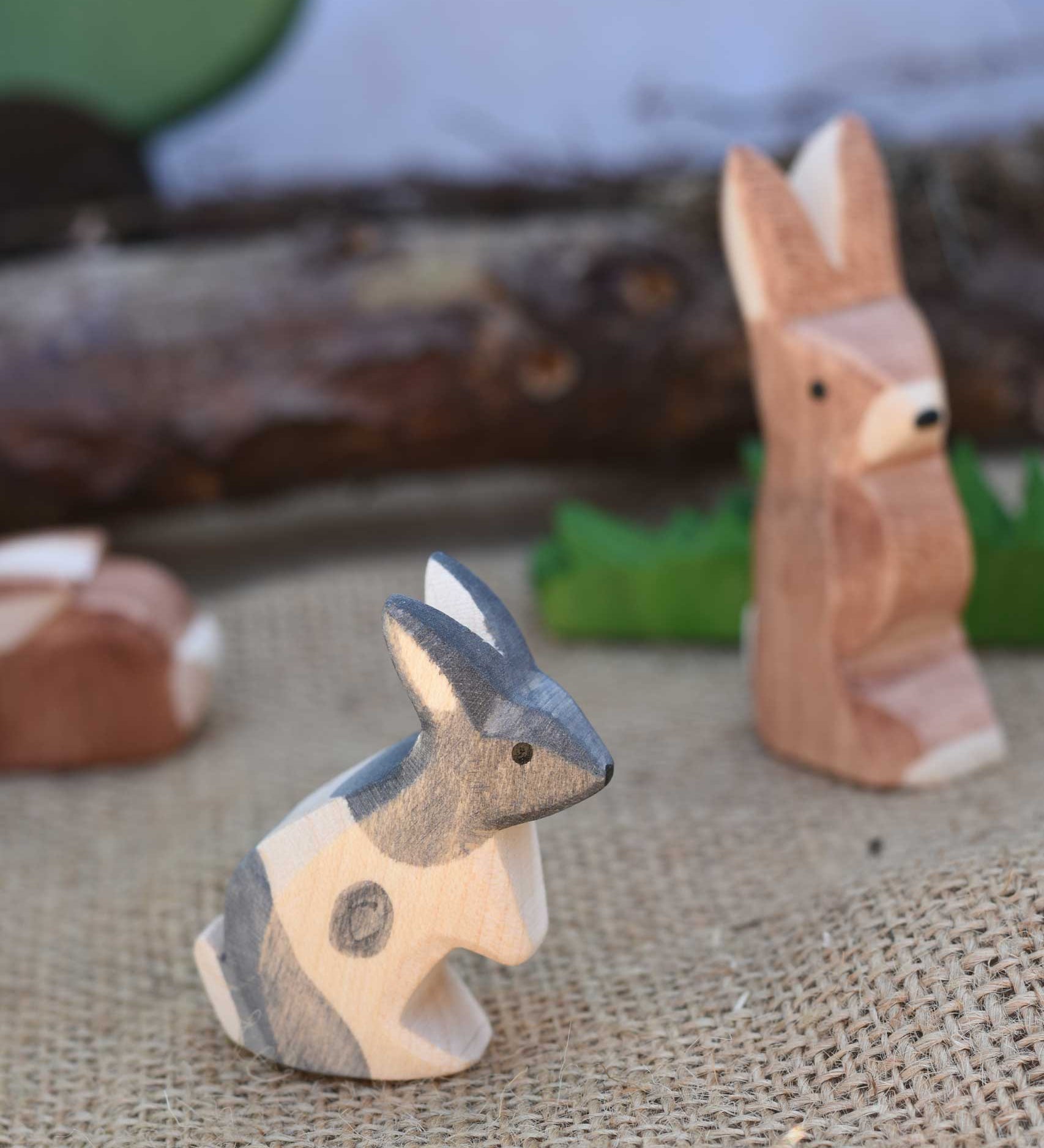 An Ostheimer Black and White Standing Rabbit wooden toy figure placed at the front of a small world play scene. Other Ostheimer rabbits can be seen in the background. Check out our full range of expertly crafted wooden toy figures and scenery here at Babipur. 