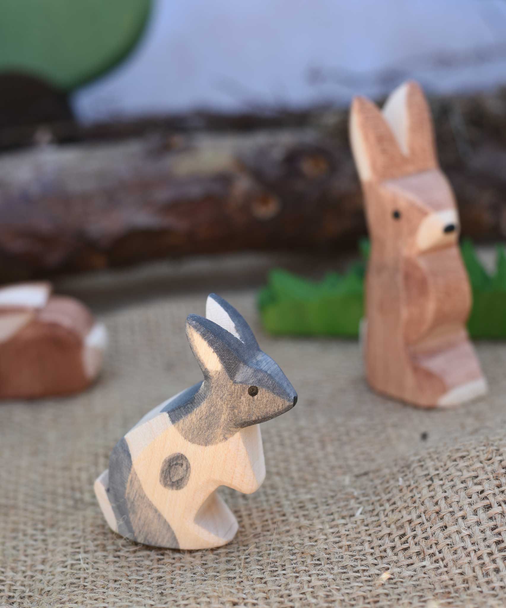 An Ostheimer Black and White Standing Rabbit wooden toy figure placed at the front of a small world play scene. Other Ostheimer rabbits can be seen in the background. Check out our full range of expertly crafted wooden toy figures and scenery here at Babipur. 