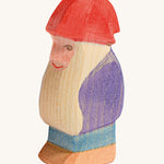 A wooden Ostheimer bodo dwarf figure wearing a purple coat, blue trousers and a red hat on a cream background.
