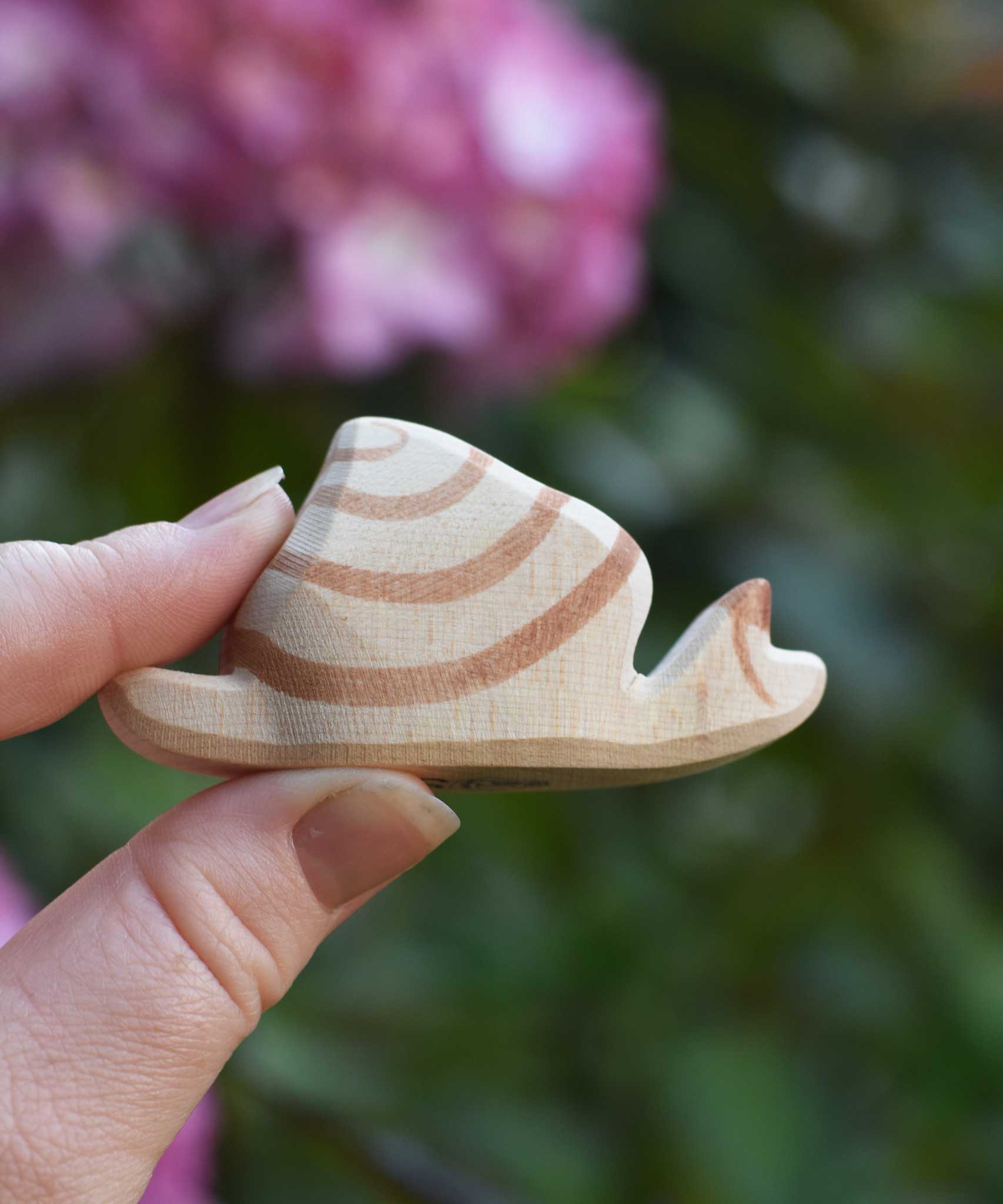 An Ostheimer snail wooden toy figure shown in a n adult's hand for scale. This to figure is part of a wide range of handmade wooden toy figures available at Babipur.