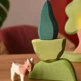 Ostheimer light, middle and dark green wooden bush scenery pieces stacked on top of each other with a small goat figure placed besides them.