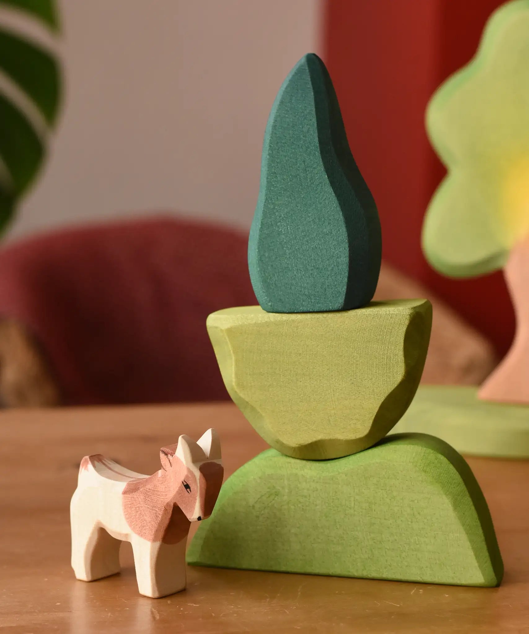 Ostheimer light, middle and dark green wooden bush scenery pieces stacked on top of each other with a small goat figure placed besides them.