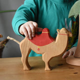 Child holding the Ostheimer camel with red saddle placing it on a wooden surface. 