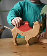 Child holding the Ostheimer camel with red saddle placing it on a wooden surface. 