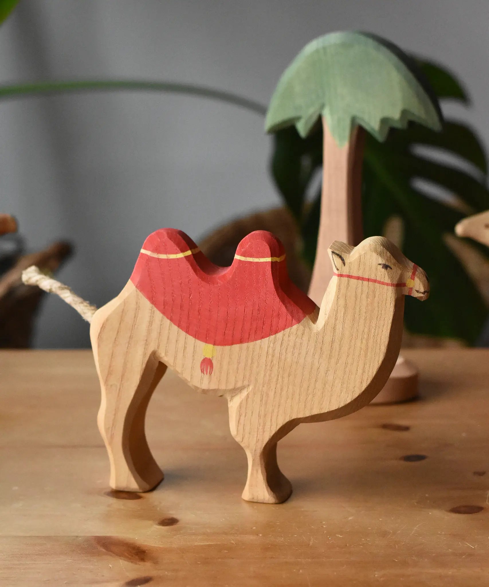 Ostheimer camel with red saddle placing it on a wooden surface with a tall palm tree figure in the background