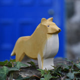 An Ostheimer Collie Dog Handmade Wooden Toy placed on a stone wall outdoors. These wooden figures are part of a large range of expertly hand crafted, Waldorf inspired, wooden toys here at Babipur.