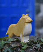 An Ostheimer Collie Dog Handmade Wooden Toy placed on a stone wall outdoors. These wooden figures are part of a large range of expertly hand crafted, Waldorf inspired, wooden toys here at Babipur.