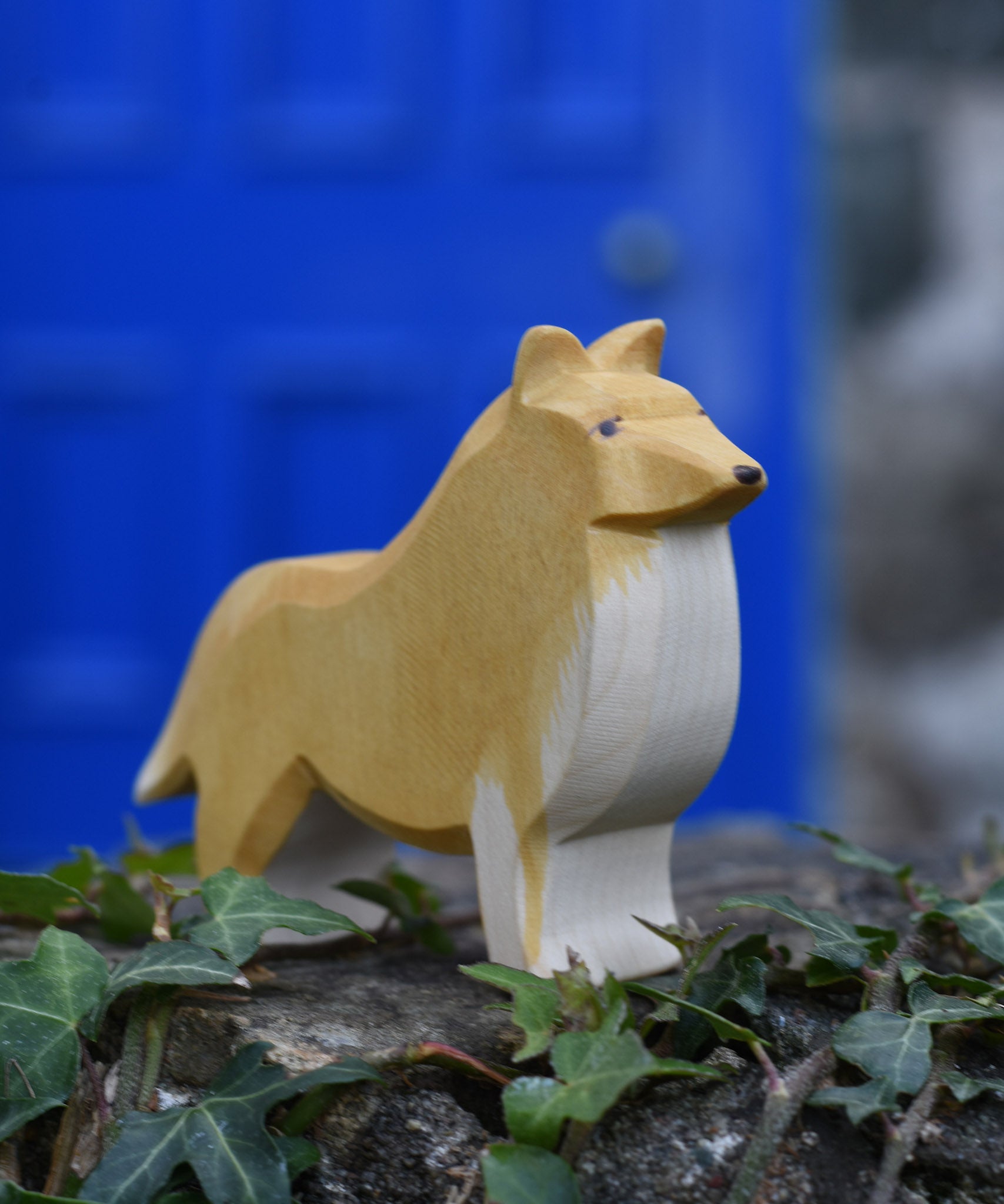 An Ostheimer Collie Dog Handmade Wooden Toy placed on a stone wall outdoors. These wooden figures are part of a large range of expertly hand crafted, Waldorf inspired, wooden toys here at Babipur.