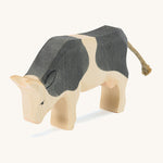 A wooden black and white Ostheimer standing cow figure on a cream background.