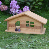 An Ostheimer wooden dolls house placed on grass with two purple Nins stood in the doorway. These wooden figures are part of a large range of expertly hand crafted, Waldorf inspired, wooden toys here at Babipur. 