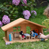 A Ostheimer wooden dolls house set up with PlanToys dolls and furniture inside. A child's hand can be seen to the side driving a Grimm's car around. These wooden figures are part of a large range of expertly hand crafted, Waldorf inspired, wooden toys here at Babipur.