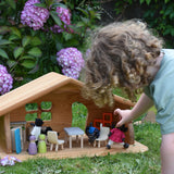 A Ostheimer wooden dolls house set up with PlanToys dolls and furniture inside. A child's hand can be seen holding one of the dolls. These wooden figures are part of a large range of expertly hand crafted, Waldorf inspired, wooden toys here at Babipur.