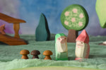 Two Ostheimer dwarves wooden toy figures placed in a small world play scene. The dwarf figures have red and green coloured outfits with matching hats and a long white beard. The figures have been placed on a green coloured Ostheimer play scarf. These wooden figures are part of a large range of expertly hand crafted, Waldorf inspired, wooden toys here at Babipur. 