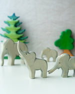 2 Ostheimer wooden elephant toy figures stood on a white table in front of some wooden Bumbu tree toys