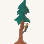 A wooden Ostheimer fir tree with a wooden Ostheimer woodpecker perched on the tree trunk on a cream background.