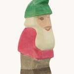A wooden Ostheimer Fridolin dwarf figure wearing a red top, brown trousers and a green hat on a cream background.