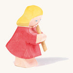 A Ostheimer wooden girl figure wearing a red dress playing a flute on a cream background.
