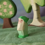 An Ostheimer green dwarf wooden toy figure placed in a small world play scene. The dwarf figure has a green coloured outfit with matching hat and a long white beard. The figure has been placed on a green coloured Ostheimer play scarf. This wooden figure is part of a large range of expertly hand crafted, Waldorf inspired, wooden toys here at Babipur. 