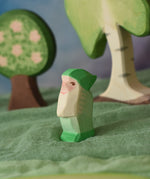 An Ostheimer green dwarf wooden toy figure placed in a small world play scene. The dwarf figure has a green coloured outfit with matching hat and a long white beard. The figure has been placed on a green coloured Ostheimer play scarf. This wooden figure is part of a large range of expertly hand crafted, Waldorf inspired, wooden toys here at Babipur. 