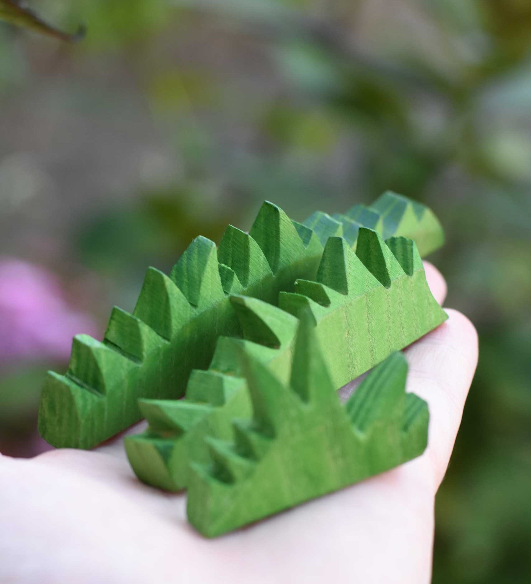 The Ostheimer Wooden green grass Figures in an adults hand. The grass comes in a set of three and are perfect for small world play scenes. 