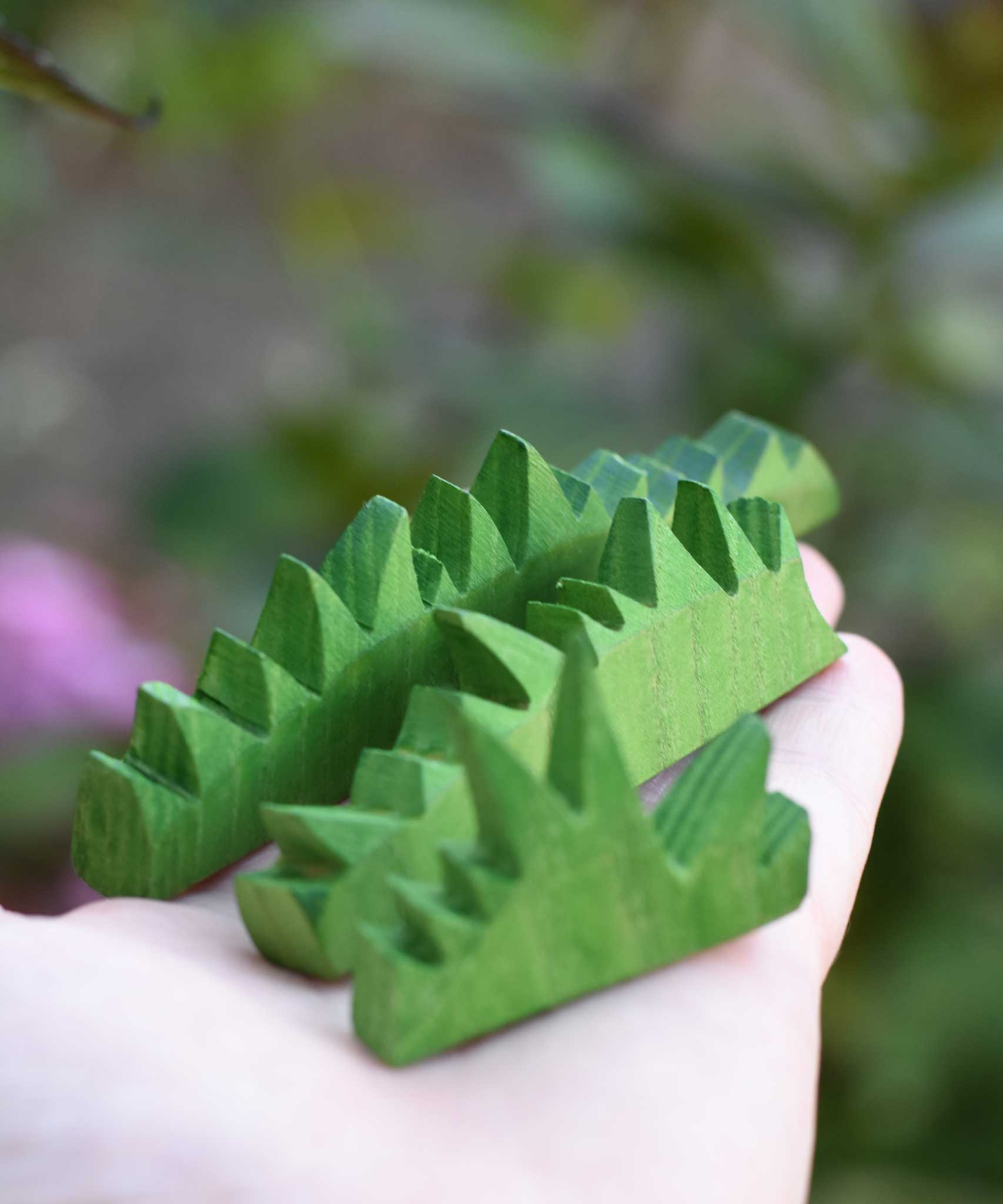 The Ostheimer Wooden green grass Figures in an adults hand. The grass comes in a set of three and are perfect for small world play scenes. 