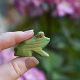 An Ostheimer Wooden green sitting frog Figure held in an adult's hand for scale. 
